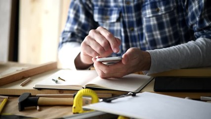 Carpenter using smartphone in small business woodwork workshop for planning a new DIY project - Powered by Adobe