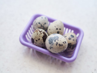 Several small spotted quail eggs lie in a small purple plastic basket.