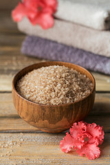 Sea salt and colorful towels with coral azalea flowers on rustic wooden background.