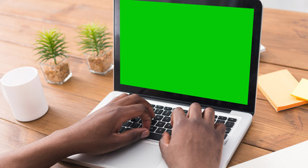 Millennial man working on laptop with blank green screen