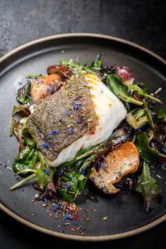 Gebratener d&auml;nischer Skrei Fisch Filet mit Steinpilzen und Salat als closeup auf einem Modern Design Teller