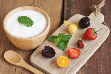Natural homemade plain organic yogurt mixed with fresh berry fruit white bowl and wood spoon on wood texture background