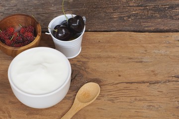 Natural homemade plain organic yogurt mixed with fresh berry fruit white bowl and wood spoon on wood texture background