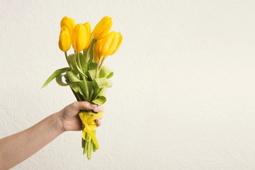 Hand holding bunch of tulips at white background, copy space