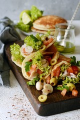Unsweetened pancakes with turkey, lettuce, tomatoes, pickled mushrooms, olives and greens in the form of tacos on a wooden board. tasty snack of their pancakes and vegetables. Healthy eating concept