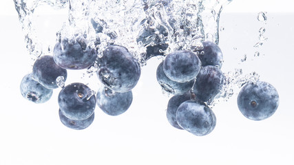 Bunch of blueberries splashing into water surface and sinking. Isolated on white background, splash...