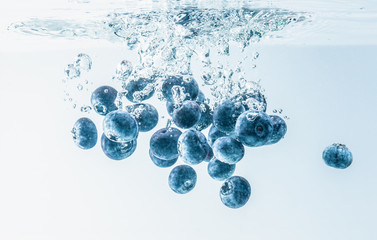 Bunch of blueberries splashing into water surface and sinking. Isolated on white background, splash...