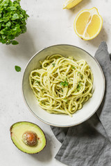 Top view on pasta with avocado and Greek basil sauce in a ceramic bowl on a white table.