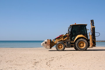 Fototapeta na wymiar yellow tractor rides on the beach along the sea