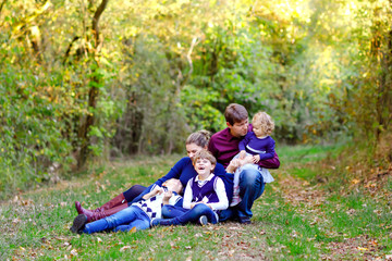 Fototapeta premium Portrait of young parents with three children. Mother, father, two kids brothers boys and little cute toddler sister girl having fun together in autumn forest. Happy family of five