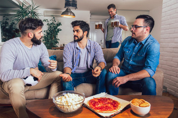 Men watching sport on tv together at home screaming cheerful. Group of friends sitting on the couch and watching a football game.