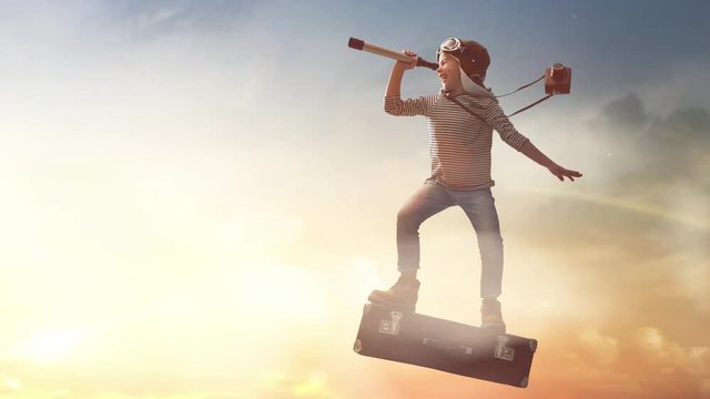 Dreams of travel! Child flying on a suitcase against the backdrop of sunset.
