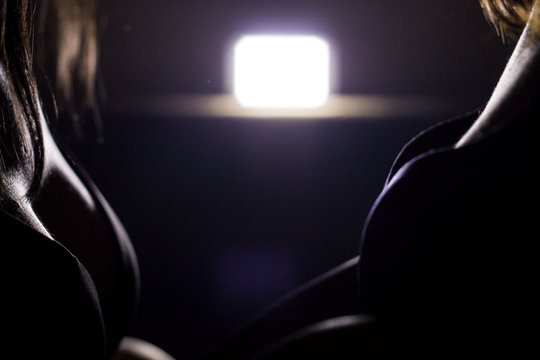 Color horizontal photo, two girls in underwear facing each other, female body part in semi-dark environment.