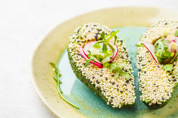 Beautiful avocado with sesame, arugula, radish and green onions. Healthy vegan food concept.
