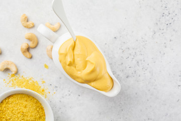 Vegan Cashew Cheese Sauce in white sauceboat, white background, top view.