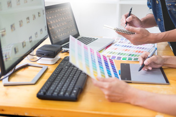 graphic designer team working on web design using color swatches editing artwork using tablet and a stylus At Desks In Busy Creative Office.