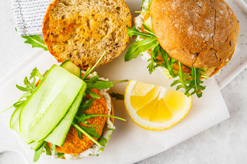 Fish burger with cucumber, arugula and mayonnaise sauce, white background, top view.