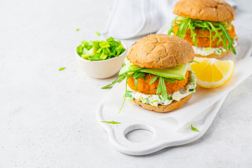 Fish burger with cucumber, arugula and mayonnaise sauce, white background, copy space.