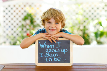 Happy little kid boy with chalk desk in hands. Healthy adorable child outdoors On desk When I grow...