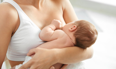 Young woman breastfeeding her baby on blurred background, closeup