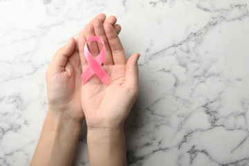 Woman holding pink ribbon on marble background, top view with space for text. Breast cancer awareness concept