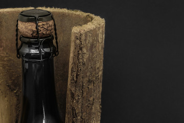 Champagne black glass bottle placed in tree bark on black background