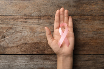 Woman holding pink ribbon on wooden background, top view with space for text. Breast cancer...