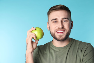 Young man with healthy teeth and apple on color background. Space for text