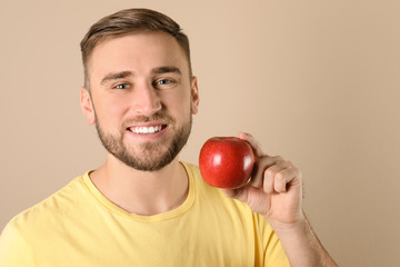 Young man with healthy teeth and apple on color background. Space for text