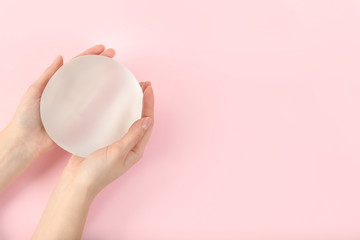 Woman holding silicone implant for breast augmentation on color background, top view with space for...