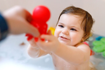 Cute adorable baby girl taking foamy bath in bathtub. Toddler playing with bath rubber toys....