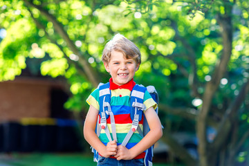 Happy little kid boy in colorful shirt and backpack or satchel on his first day to school or...