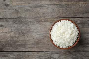 Boiled rice in bowl on wooden background, top view with space for text
