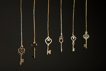 Fototapeta na wymiar Bronze vintage ornate keys hanging on threads against dark background