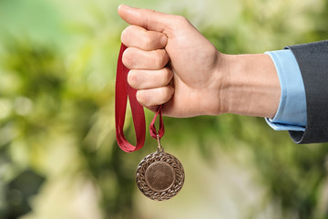 Fototapeta na wymiar Man holding gold medal on blurred background, closeup