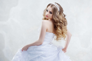 Fototapeta na wymiar Charming young bride with luxury hairstyle. Beautiful woman in wedding dress. Hairstyle with fluffy curls.