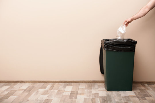Young woman throwing plastic bottle in trash bin indoors, space for text. Waste recycling