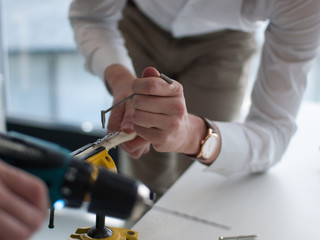 Two young doctors train how to heal fracture of radius by surgical method with use of compression plate fixation. Training performed on plastic model of bone. Photo of hands in action during drilling.