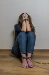 Hostage girl sitting on the floor with arms and legs chained in chains