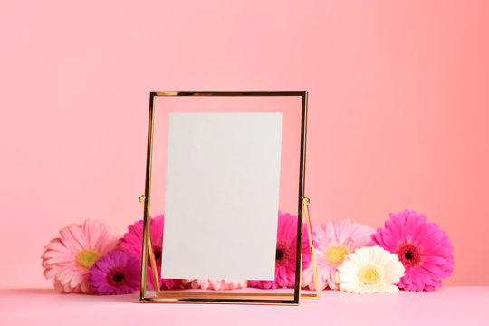 Stylish photo frame and beautiful flowers on table against color background, space for text