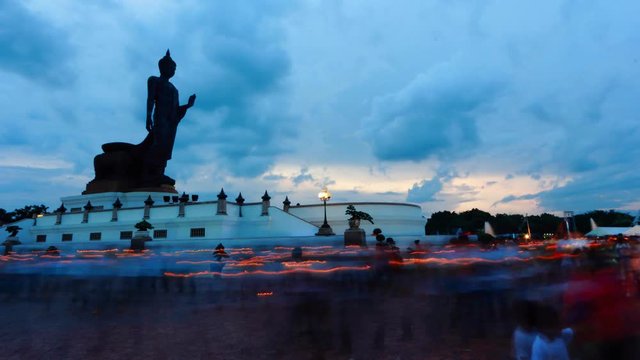 People walks with lighted candles in hand around buddha image