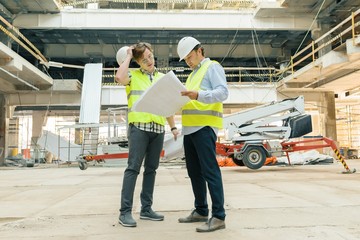 Male building workers working at construction site, builders looking in blueprint. Building,...