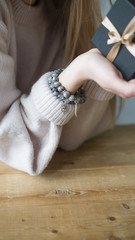 girl holds a gift box tied with a ribbon, on her arm are two tourmaline bracelets, a bracelet made...