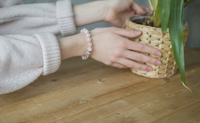 the girl on her arm has a bracelet made of pink stones (quartz), a bracelet made of quartz, hands, indoor flowers (horizontally, light toned).