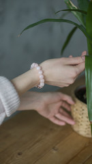 the girl on her arm has a bracelet made of pink stones (quartz), a bracelet made of quartz, hands, indoor flowers (vertically, close up).
