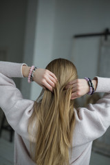 the girl straightens her blonde hair, four bracelets of purple, pink, gray, stones on the hand, bracelets of amethyst, rose quartz, tourmaline quartz, sherl, charoite (vertically).