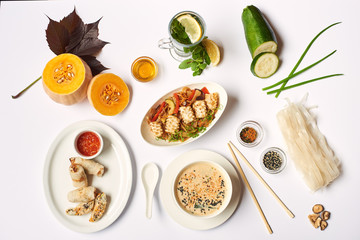 Flat lay of oriental dinner from soup with seeds, tempura shrimps and noodles with vegetables preparing for client. Three dishes lunch with mint tea ready for eating on white tablecloth.