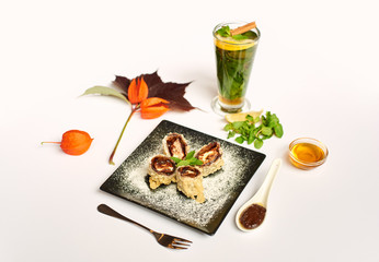 View of fresh oriental dessert on black plate decorated with physalis. Sweet sushi roll cooking prepared for client in oil with chocolate sauce and icing sugar doing by special recipe.
