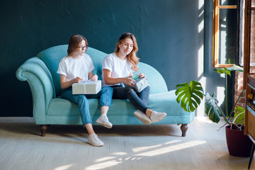 Obraz premium Two young girls, friends sitting on the sofa and packing present boxes. Holiday gift concept. Beauty box. Small business