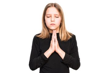 A teen girl with a serious face and eyes closed prays to God on a light background